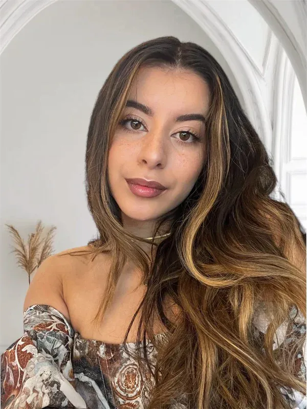 Charmain, make-up artist en eigenaar van Studio Urban Gems, met lang bruin golvend haar met highlights en glanzende rozé lippen voor een witte boog