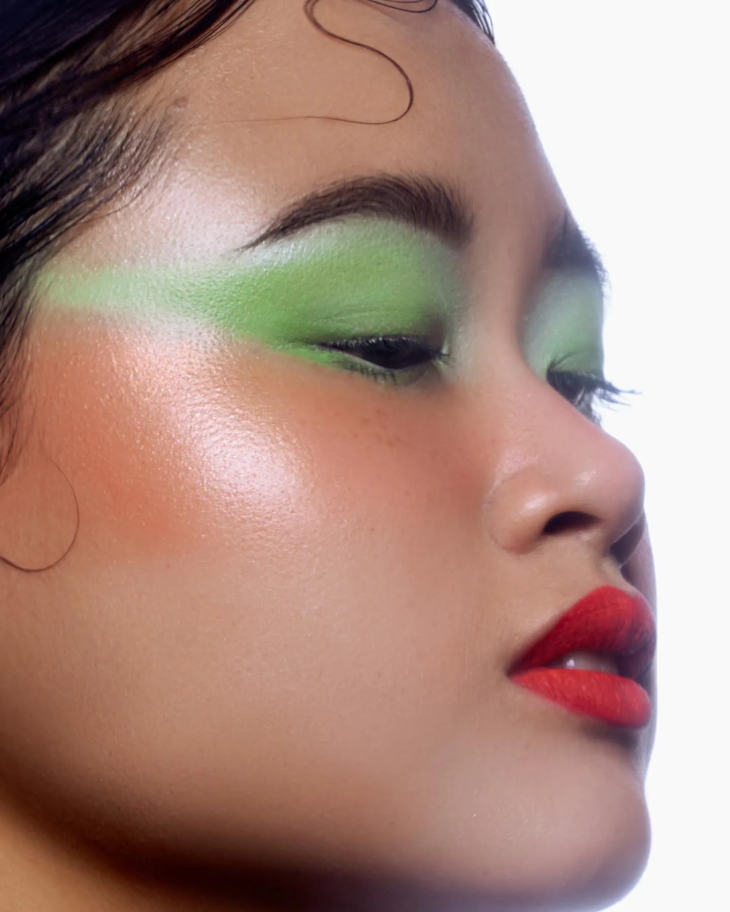 Geairbrushte limoengroene oogschaduw, koraalblush en mat rode lippen in profiel