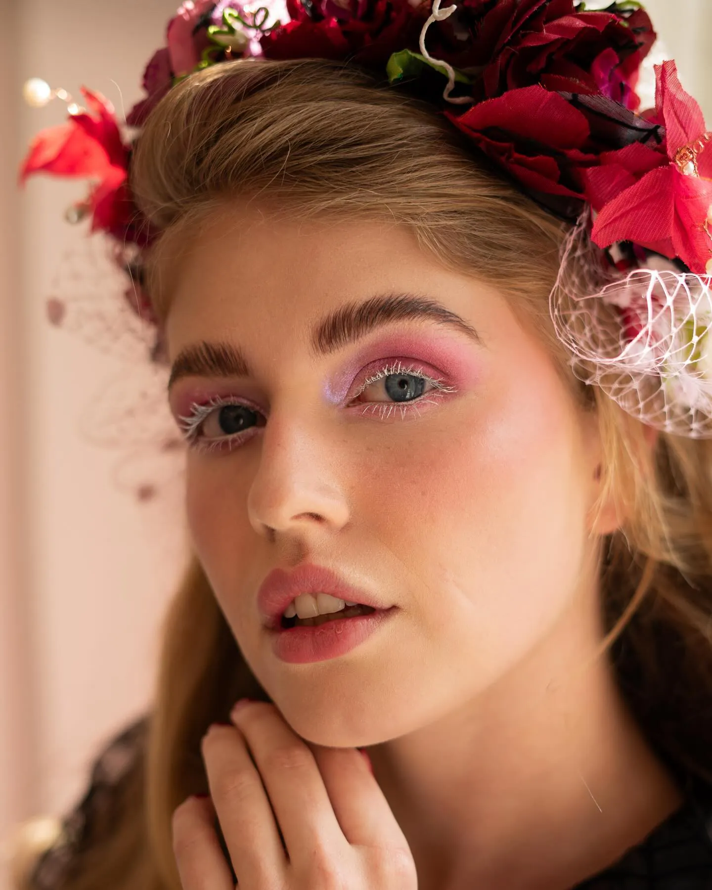 Beauty close-up met roze oogschaduw, witte mascara en blush onder een krans van rode bloemen