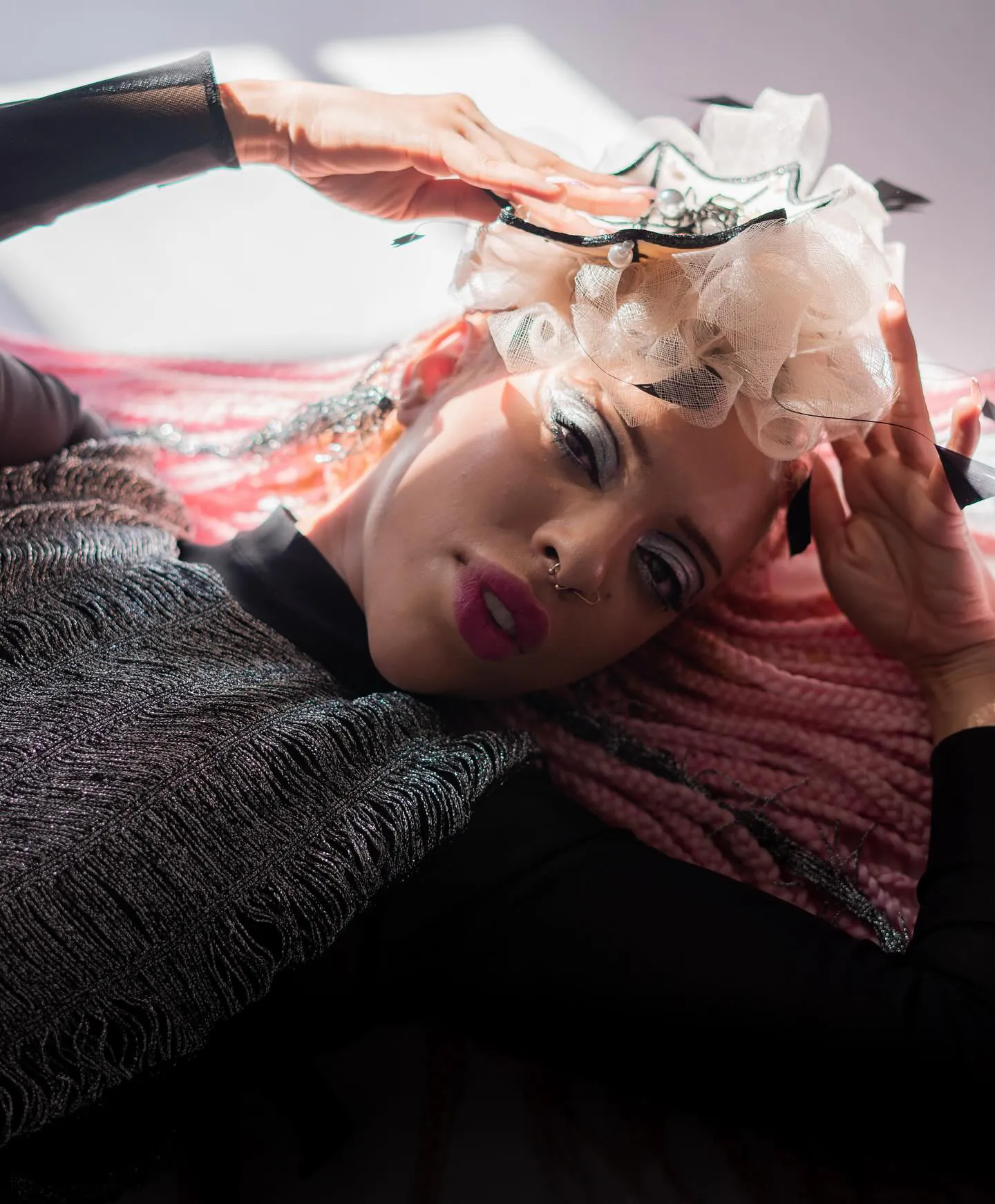 Liggend model in hard zonlicht met zilveren glitter-smokey eye, bessenrode lippen en roze vlechten