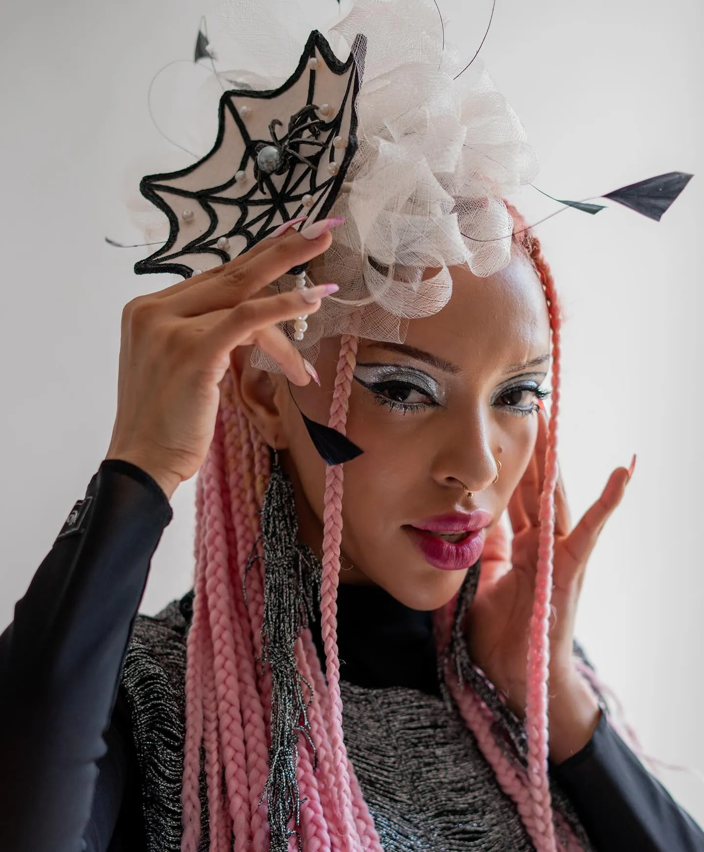 Model met zilveren grafische eyeliner en glitter, roze vlechten en een fascinator met spinnenweb en parels