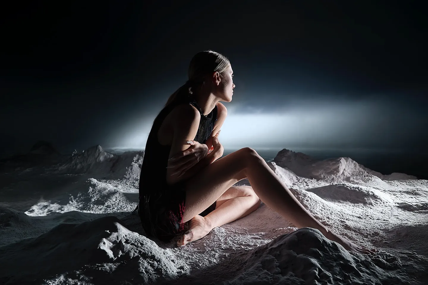 Model zit in een maanlandschap en kijkt in een horizontale lichtbundel, dramatisch tegenlicht