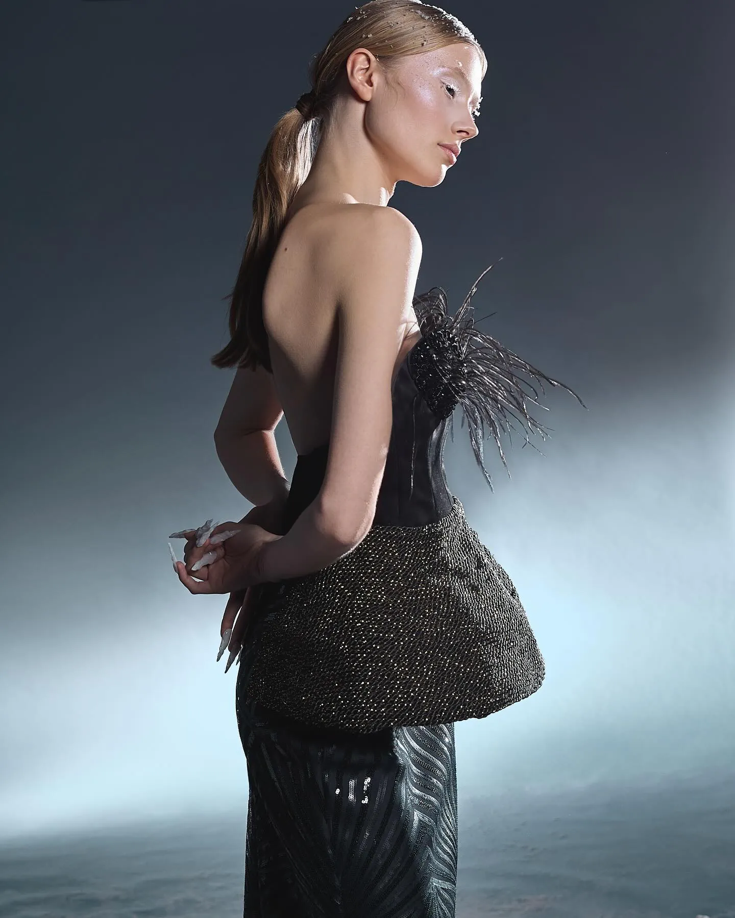 Model in zwart korset met veren en pailletten, kijkt over haar schouder, rijp in het haar