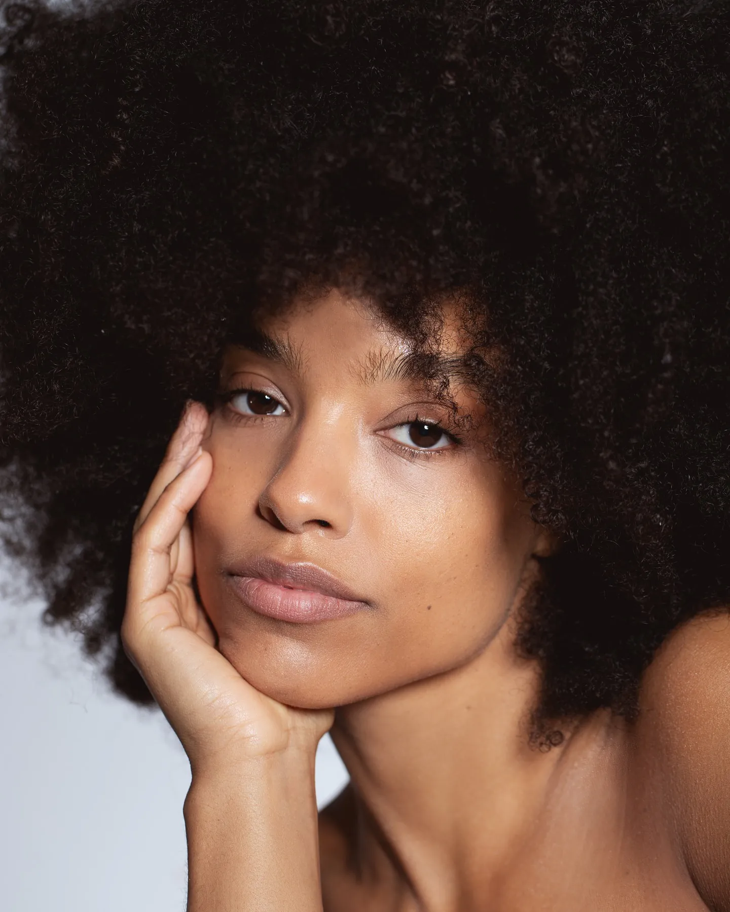 Natuurlijke no-make-up make-up: stralende huid, grote afro, hand tegen de wang