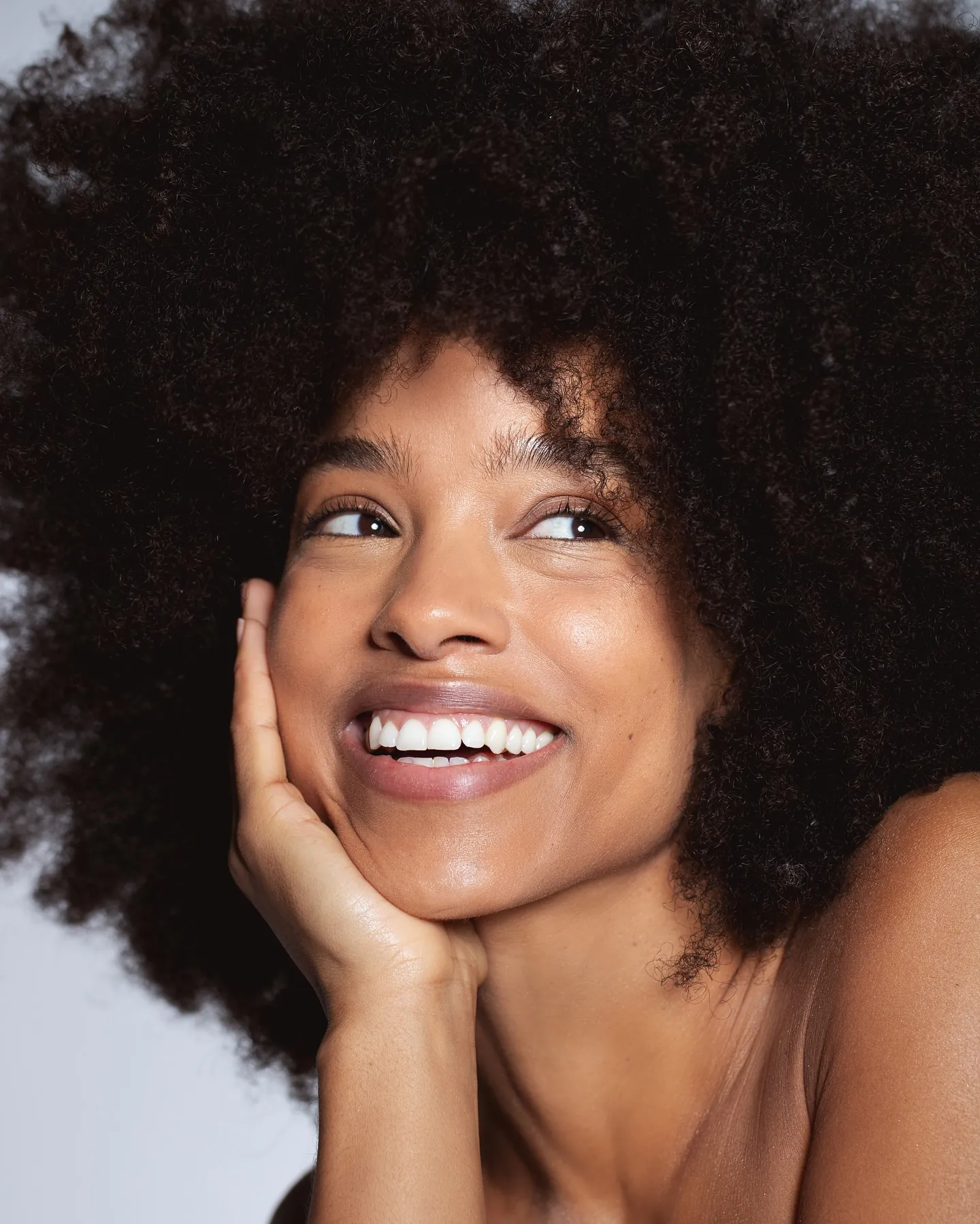 Lachende vrouw met afro en stralende natuurlijke make-up kijkt omhoog