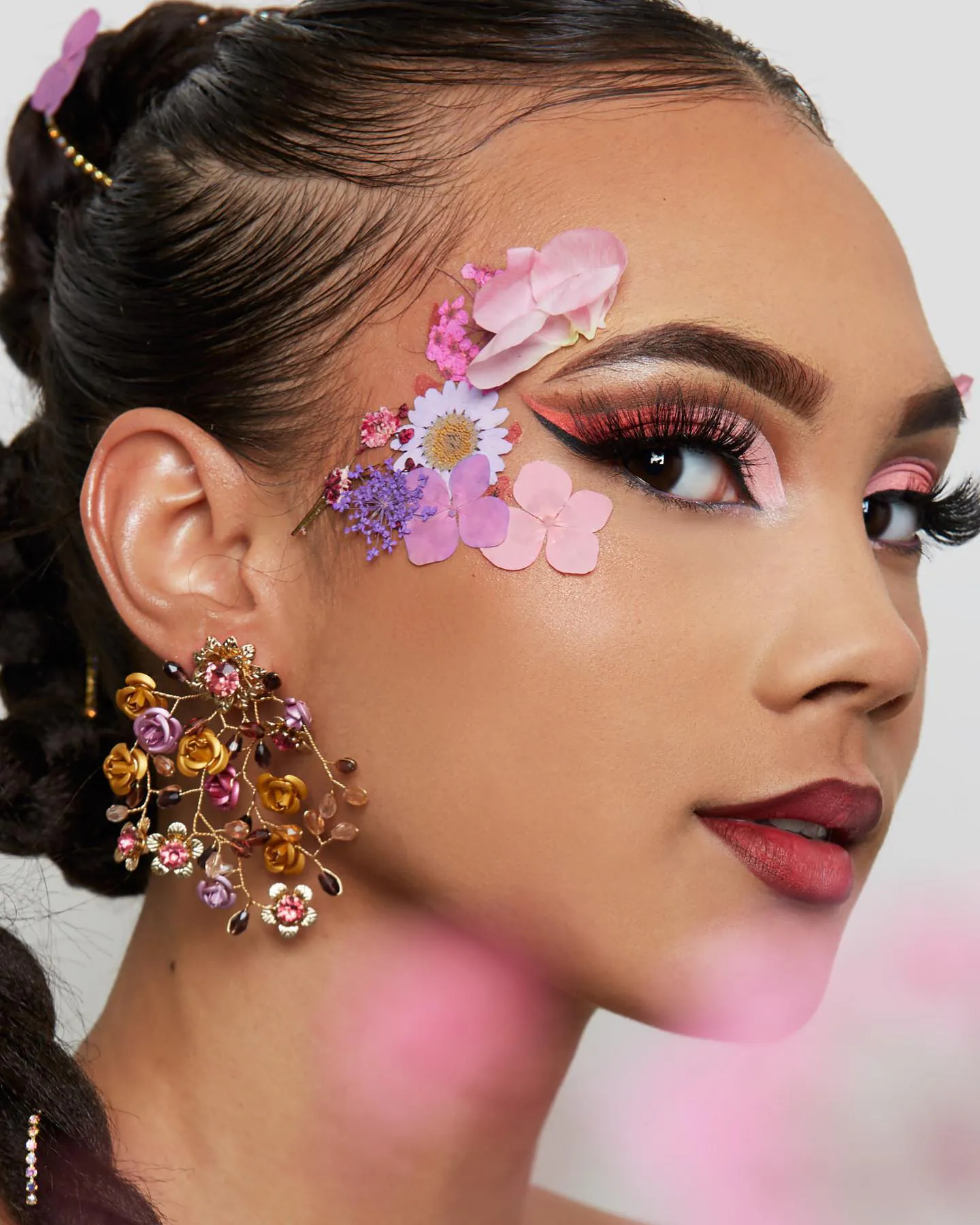 Make-up met gedroogde bloemen op de slaap, koraalroze cut crease met eyeliner en bessenrode lippen
