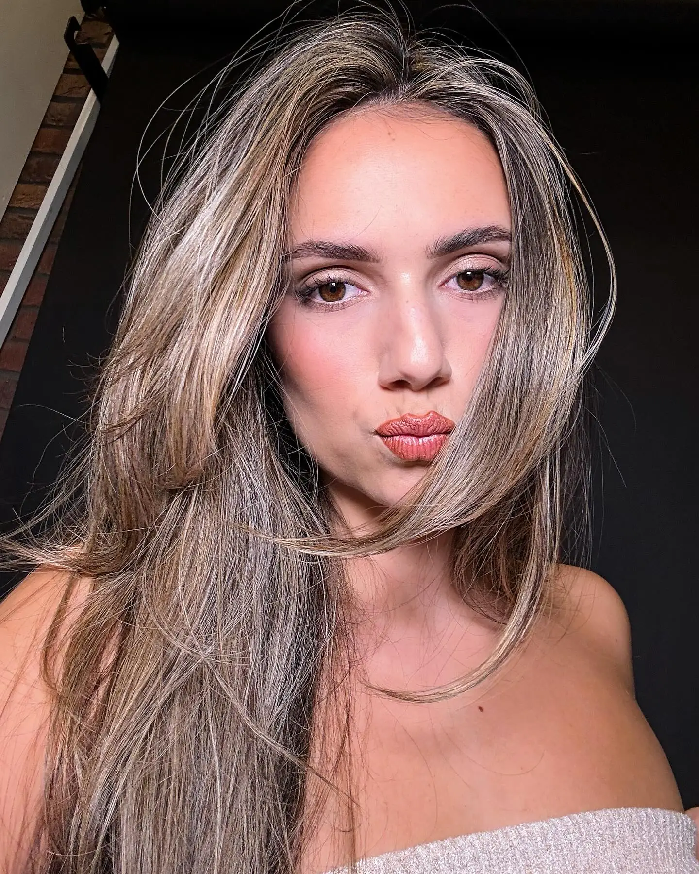 Glam make-up met glanzende lippen, haar deels voor het gezicht, in de studio met bakstenen muur