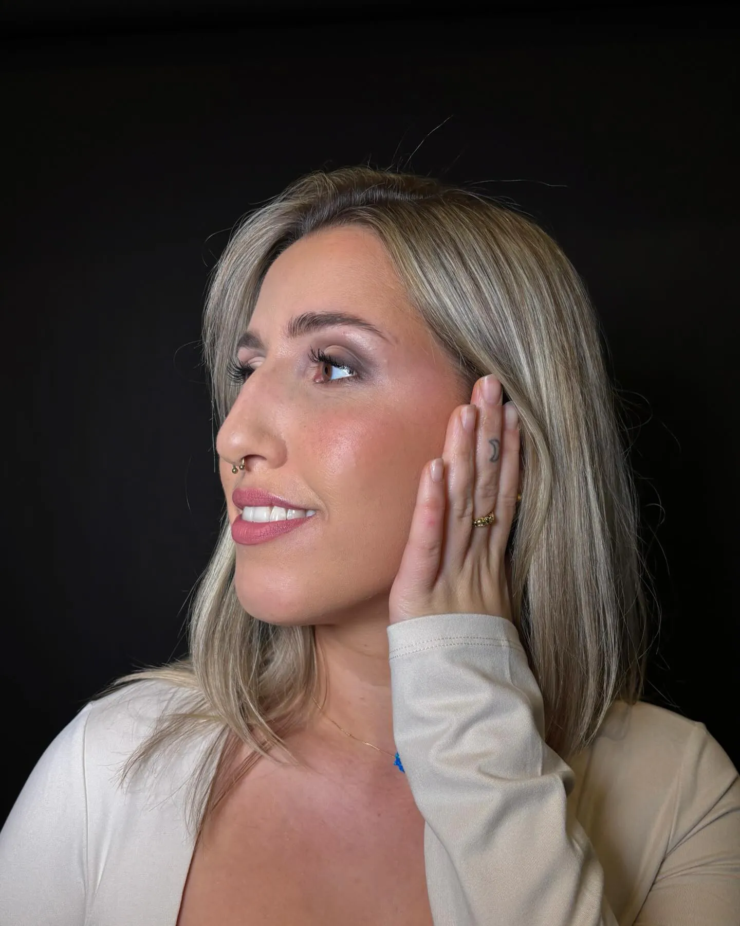 Vrouw met soft glam make-up en blond haar lacht in profiel, hand bij haar oor