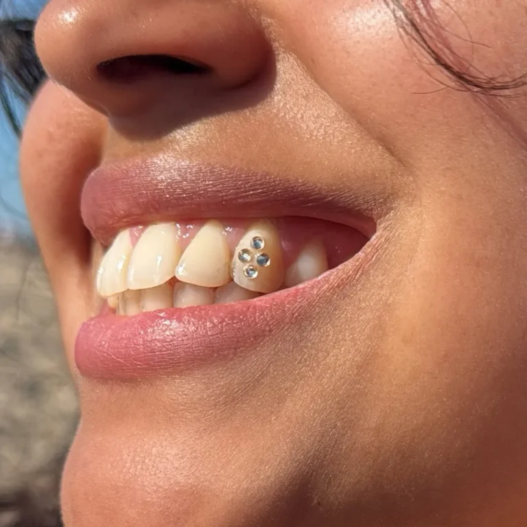 Detail van een glimlach met een tooth gem van vier kristallen op de snijtand, glanzende roze lippen