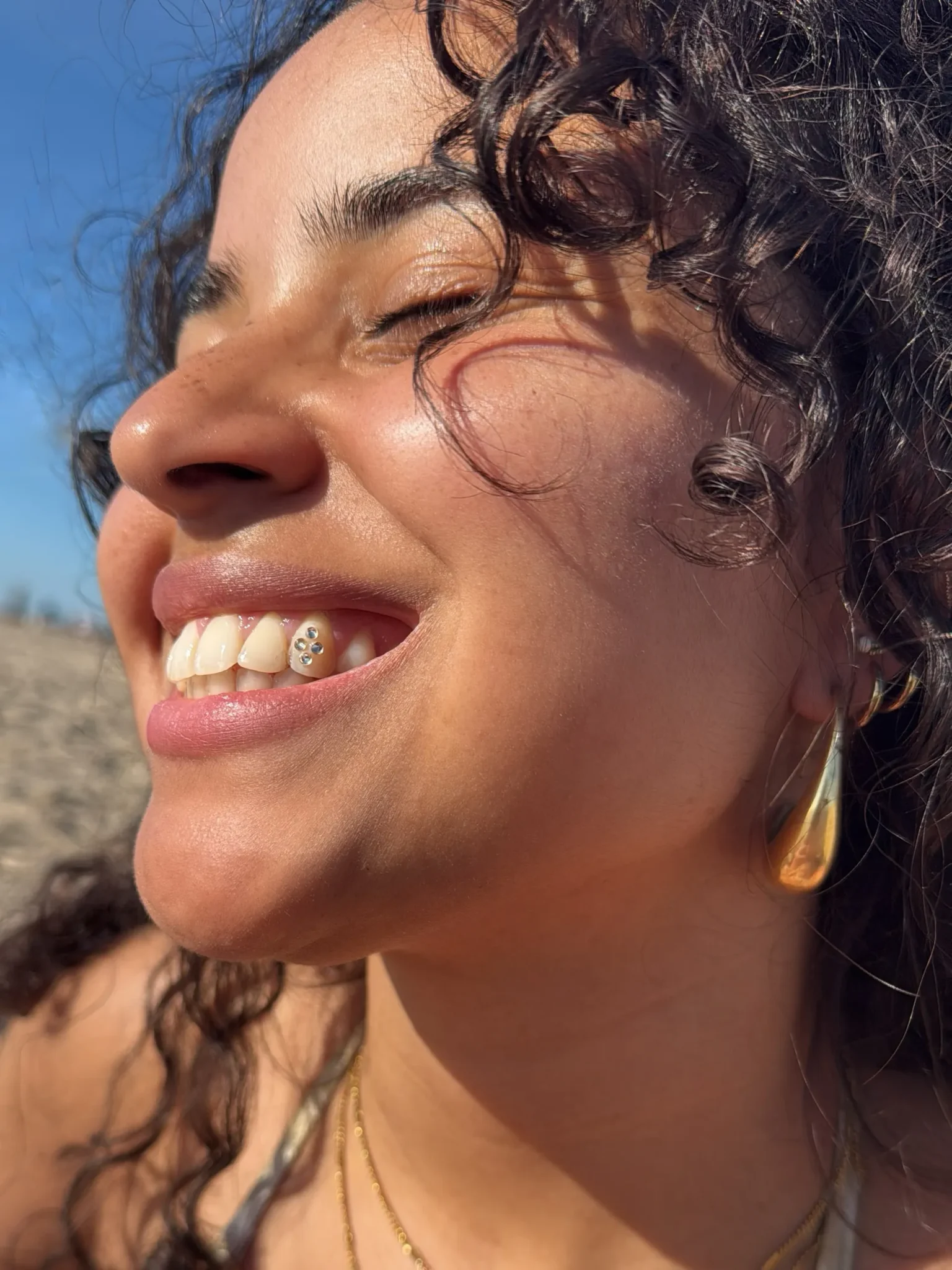 Lachende vrouw met krullen in de zon, met een tooth gem van vier kleine kristallen op haar snijtand
